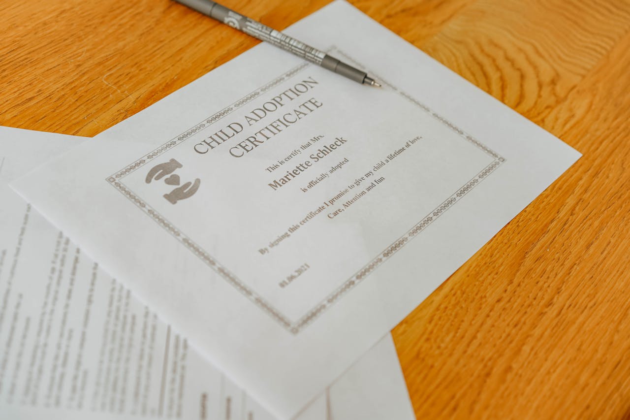 Close-up of a child adoption certificate and documents with a pen on a wooden table.